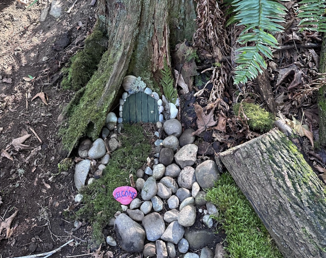 a tree stump decorated with a small door and path with rocks and moss to create a fairy home